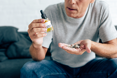 cropped view of man in t-shirt holding pills and cannabis oil