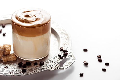 delicious Dalgona coffee in glass near coffee beans, brown sugar on silver platter on white background