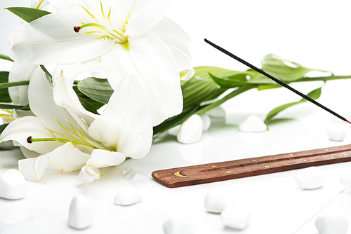 aroma stick on wooden stand near lilies on white background