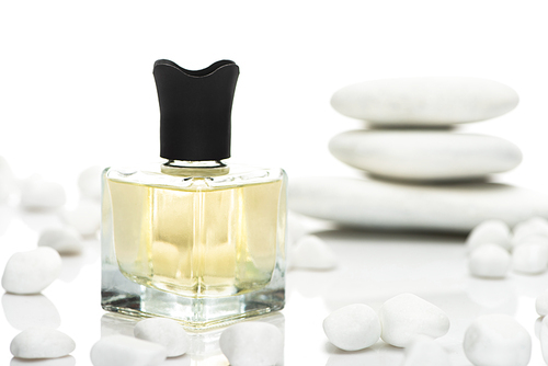 selective focus of home perfume in bottle near spa stones on white background
