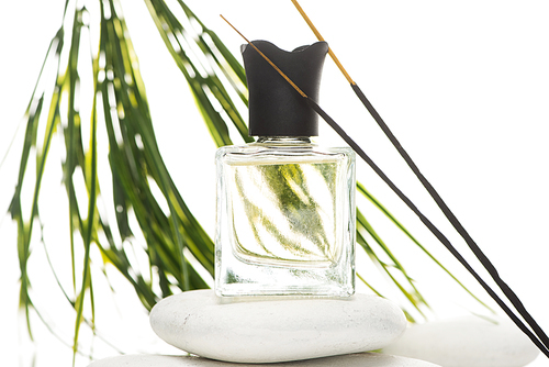 selective focus of aroma sticks near perfume in bottle on spa stone on white background