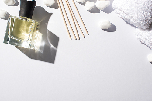top view of aroma sticks with perfume in bottle near spa stones and towel on white background