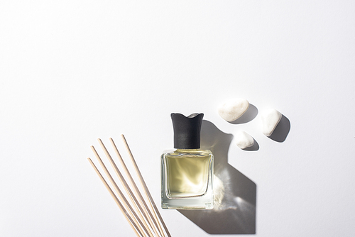 top view of aroma sticks with perfume in bottle near stones on white background