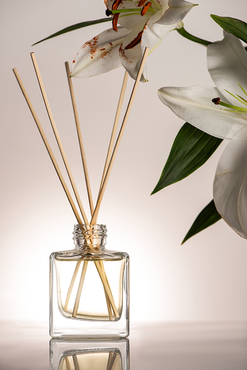 wooden sticks in perfume in bottle near lily flowers on beige background