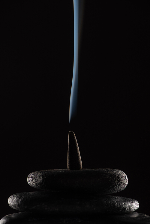 burning incense cone with smoke on stones on black background