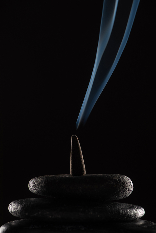 burning incense cone with smoke on stones on black background