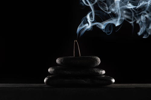 burning incense on stones with smoke on black background