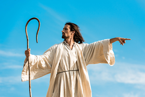 man in jesus robe holding wooden cane and pointing with finger