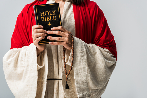 cropped view of man holding holy bible and rosary breads isolated on grey