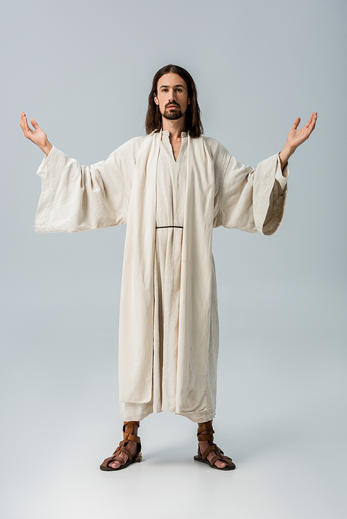 bearded man in jesus robe standing with outstretched hands on grey