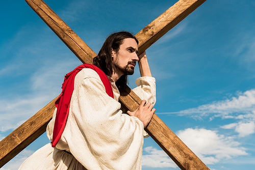 low angle view of bearded man holding cross against blue sky