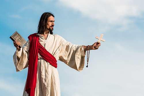 jesus holding holy bible and cross against blue sky with clouds