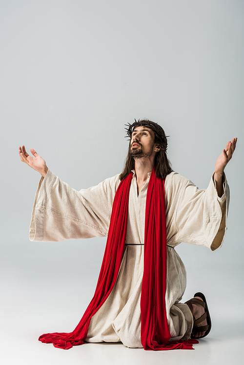 bearded man in wreath praying on knees with outstretched hands on grey