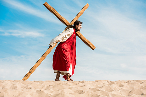 bearded man in wreath walking with cross in desert