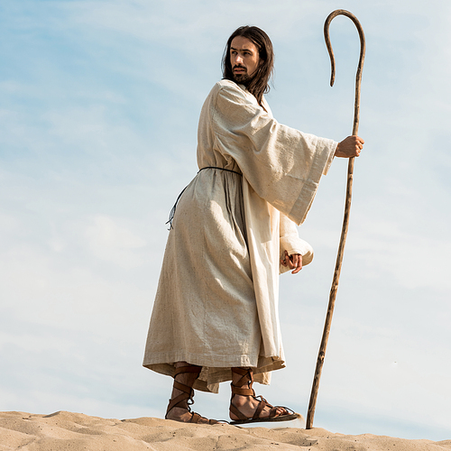 low angle view of man walking with wooden cane in desert