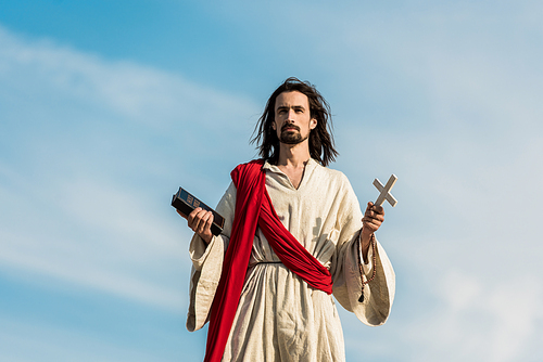 jesus holding cross and holy bible against blue sky with clouds