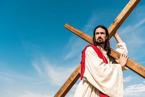 low angle view of bearded jesus holding cross against sky with clouds