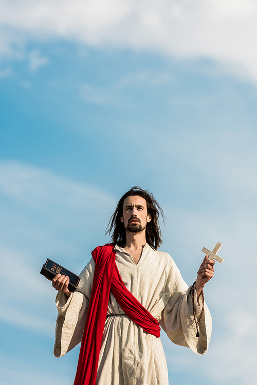 jesus holding holy bible and cross against blue sky with clouds