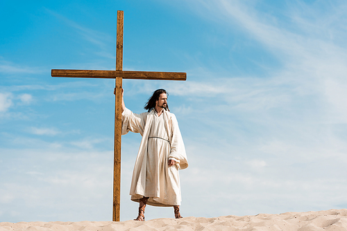 handsome bearded man standing with wooden cross in desert