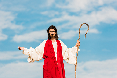 handsome man in wreath with outstretched hands holding cane