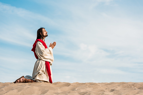 man praying on knees in desert on golden sand