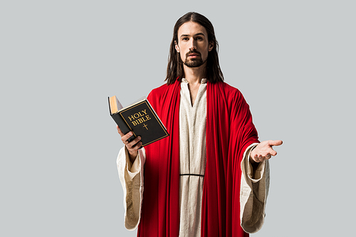 handsome man gesturing and holding holy bible isolated on grey