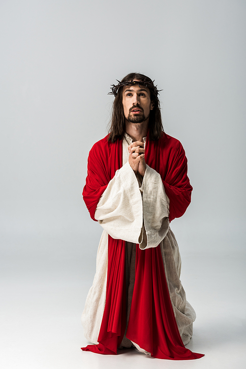 handsome man in wreath with spikes praying on knees on grey