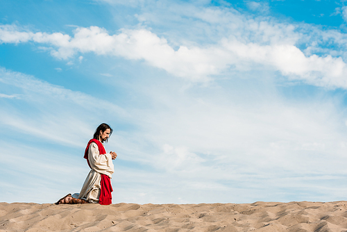 man praying on knees with clenched hands in desert