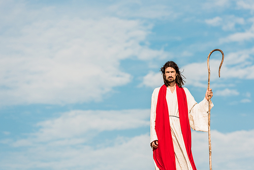 handsome bearded man holding wooden cane and standing outside