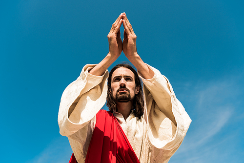 low angle view of jesus with praying hands against blue sky