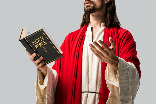 cropped view of religious man in jesus robe holding holy bible and gesturing isolated on grey