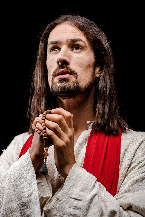 bearded man praying while holding rosary beads isolated on black