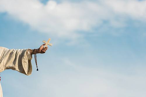 cropped view of religious man holding cross and rosary beads against blue sky