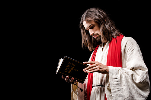 religious man holding book with holy bible lettering isolated on black