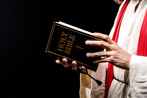 cropped view of man holding book with holy bible letters isolated on black