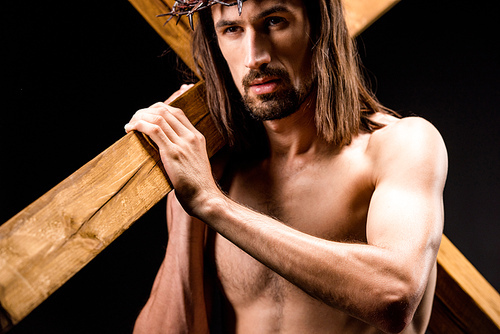 religious and shirtless man in wreath with spikes holding wooden cross isolated on black