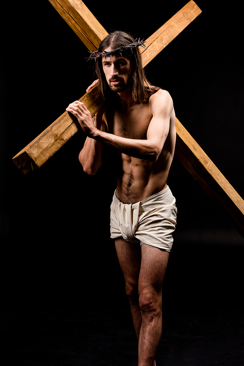 bearded shirtless man in wreath holding wooden cross isolated on black