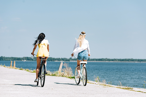 back view of blonde and brunette girls riding bikes near river in summer