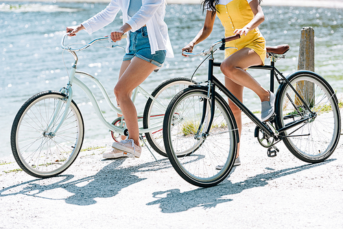 cropped view of girls riding bikes near river in summer