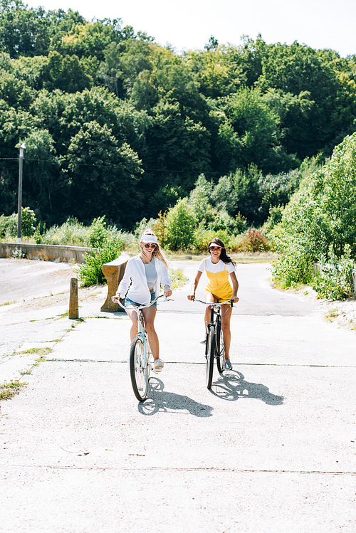 happy blonde and brunette girls riding bikes in summer