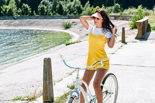smiling brunette beautiful girl riding bicycle near river in summer