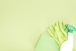 top view of green rubber gloves, rag and spray bottle on green background