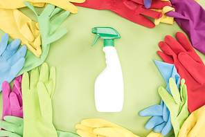 top view of multicolored rubber gloves in circle with spray bottle with detergent in center on green background