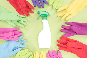 top view of multicolored rubber gloves in circle around spray bottle with detergent on green background
