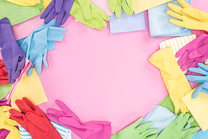 top view of messy scattered multicolored rags and rubber gloves on pink background with copy space