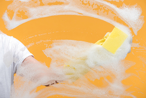 cropped view of cleaner in rubber glove cleaning glass with sponge on orange background