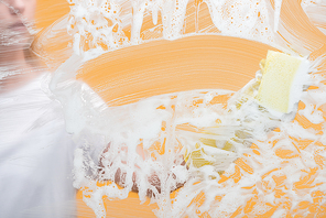 cropped view of young woman in rubber glove with sponge cleaning glass covered with foam