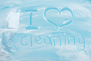 cropped view of cleaner with sponge near i love cleaning handwritten lettering on glass with white foam on blue background