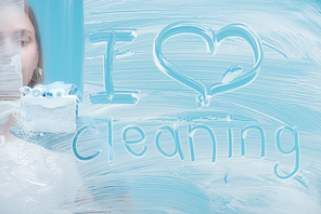 partial view of woman cleaning glass with sponge near i love cleaning lettering written on white foam on blue background