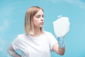 young woman in rubber glove cleaning glass with rag on blue background